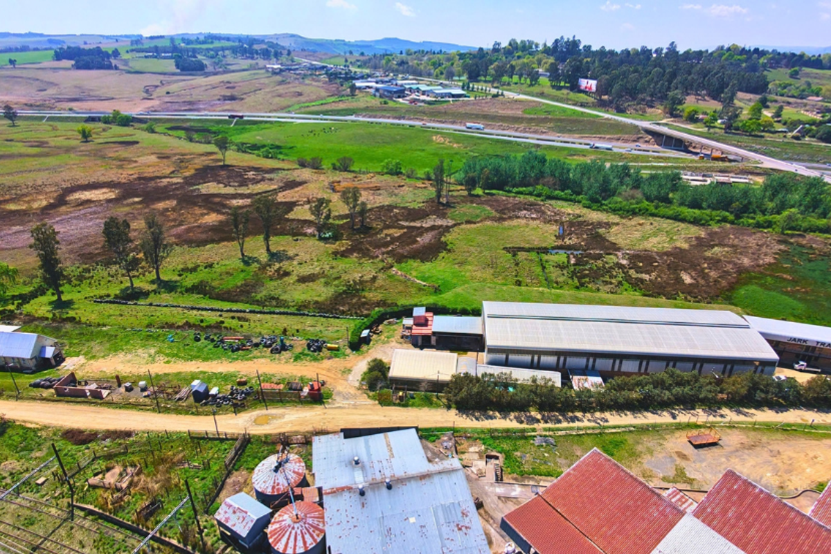 Aerial view of a commercial property featuring a large industrial warehouse, silos, and extensive surrounding land with highway access.