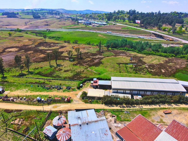 Aerial view of a commercial property featuring a large industrial warehouse, silos, and extensive surrounding land with highway access.