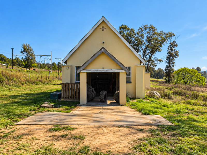 A detached commercial building featuring a gabled roof, concrete entrance pad, and rural surroundings.