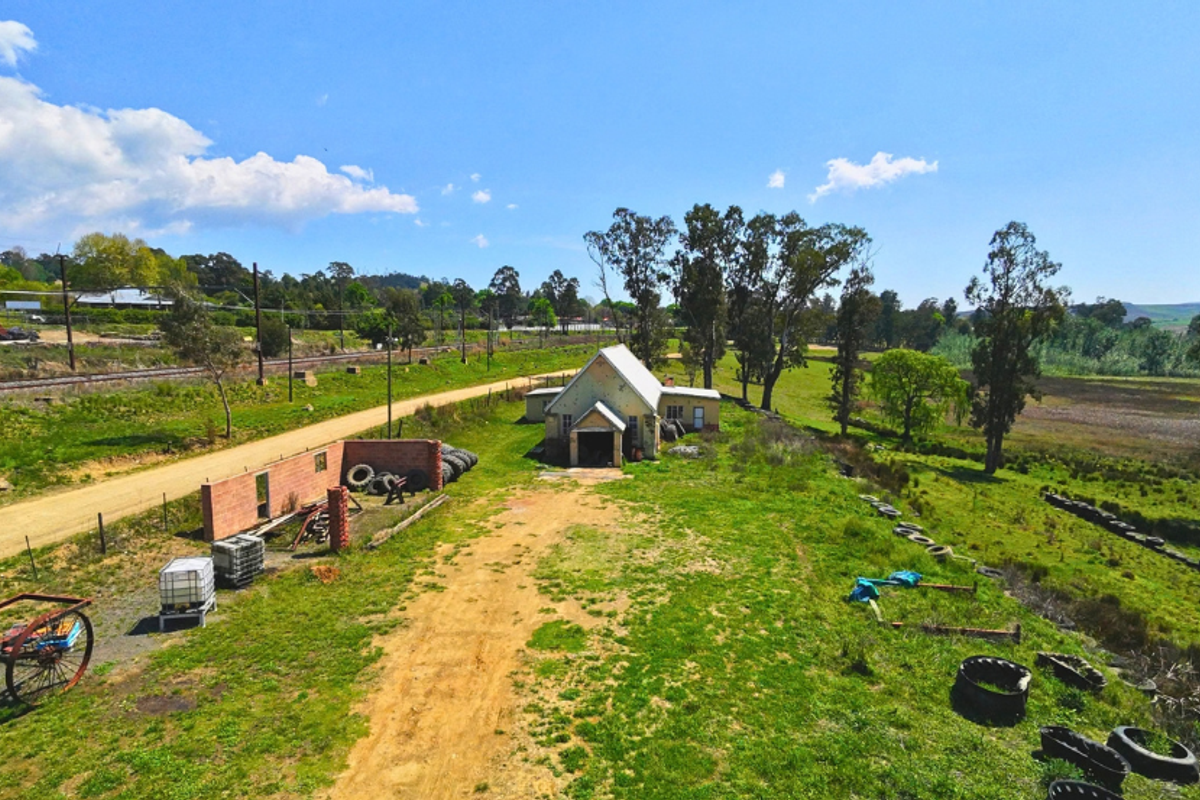 Aerial view of a commercial property featuring a standalone building, brick boundary wall, and surrounding land with access road.