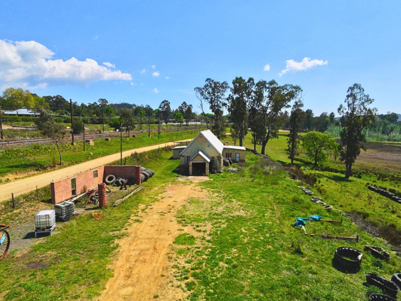 Aerial view of a commercial property featuring a standalone building, brick boundary wall, and surrounding land with access road.