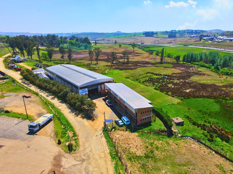 Aerial view of a commercial property featuring two industrial warehouse buildings, paved access roads, and surrounding open land.
