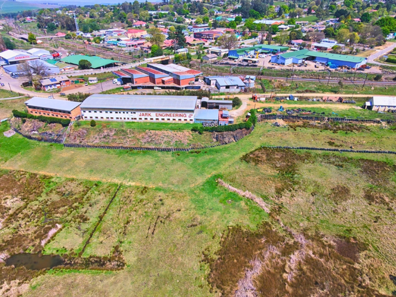 Aerial view of a commercial industrial facility featuring large warehouse structures, metal roofing, and surrounding land in a semi-rural setting.