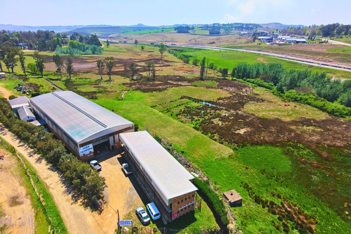 Aerial view of an industrial property featuring two warehouse structures, gravel access areas, and surrounding open land with highway access.