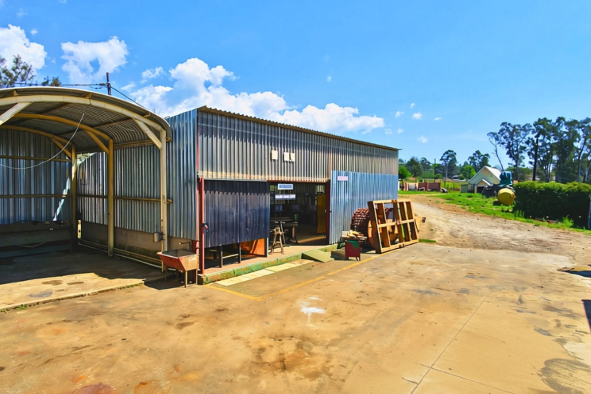 Industrial workshop building featuring corrugated metal cladding, a steel-framed covered area, and a concrete yard space suitable for operational use.