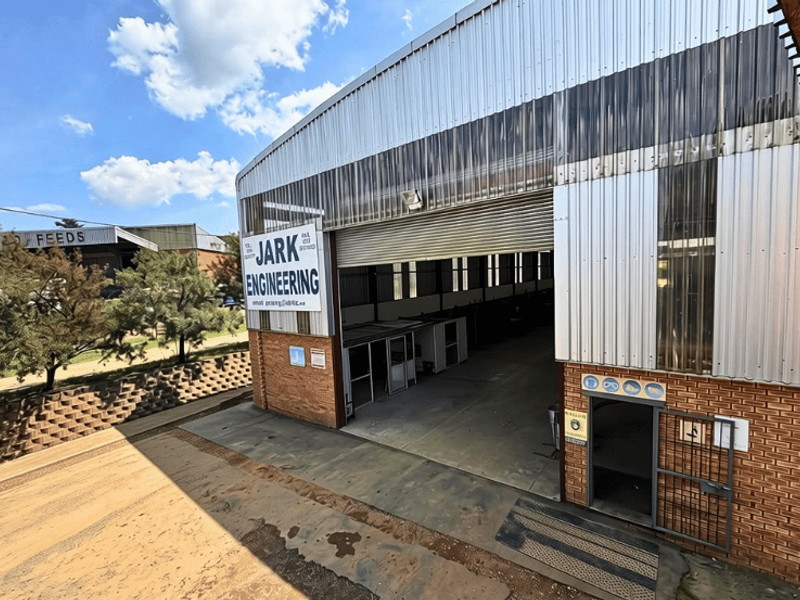 Industrial warehouse facility featuring a large roller shutter entrance, corrugated metal cladding, and brick exterior construction with an adjacent retaining wall.