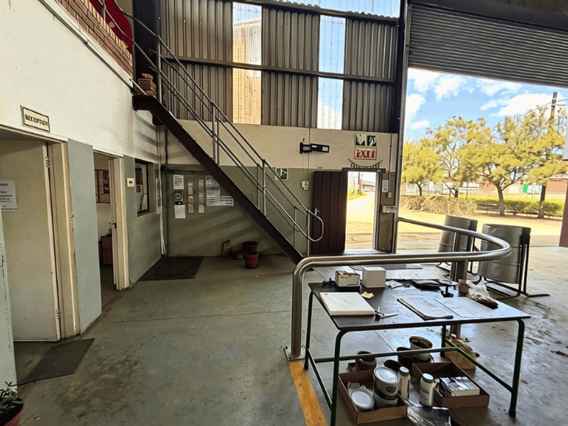 Industrial warehouse utility space featuring a metal staircase, concrete flooring, and a large roller shutter door providing access to the exterior.