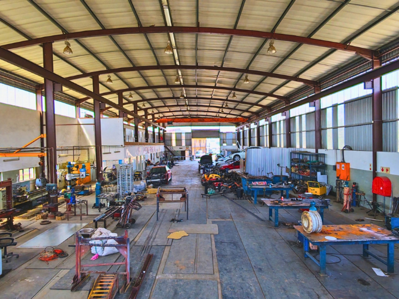 Spacious industrial workshop featuring a high-clearance steel portal frame, concrete flooring, overhead crane infrastructure, and ample natural light through translucent wall panels.