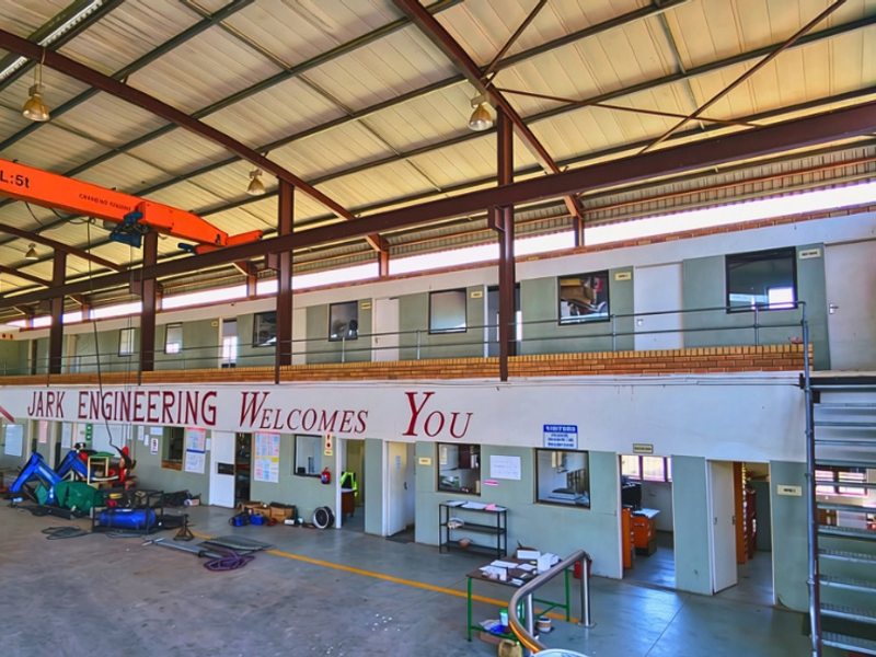 Spacious industrial workshop featuring a high-clearance ceiling with an overhead gantry crane, mezzanine office level, and integrated ground-floor workspace.