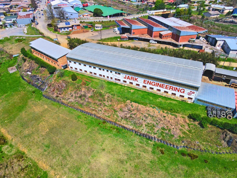 Aerial view of an industrial facility featuring a large warehouse building with corrugated metal roofing and surrounding grounds.