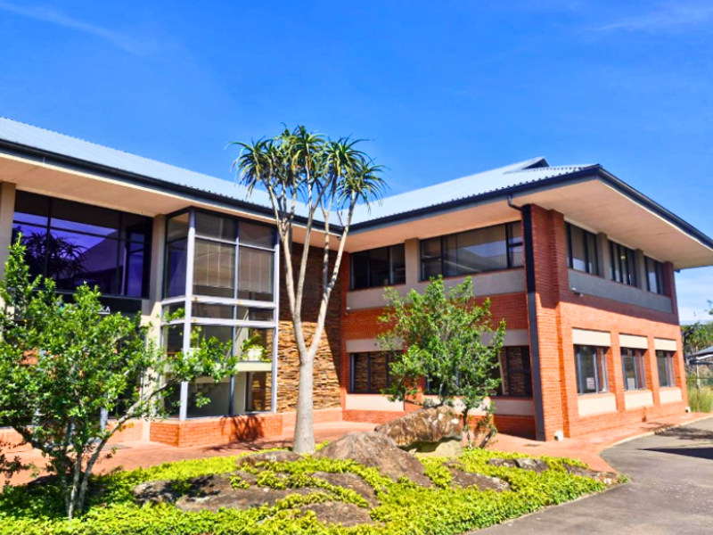 A professional office building featuring a combination of face brick and stone cladding, large glass windows, and a well-maintained landscaped entrance area.