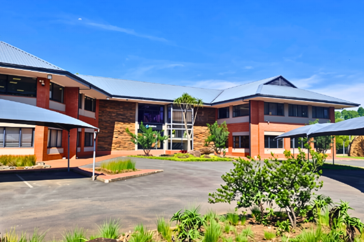 A professional exterior view of a modern office building featuring brick cladding, metal roofing, and dedicated shaded parking areas within a landscaped setting.