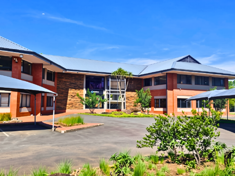 A professional exterior view of a modern office building featuring brick cladding, metal roofing, and dedicated shaded parking areas within a landscaped setting.