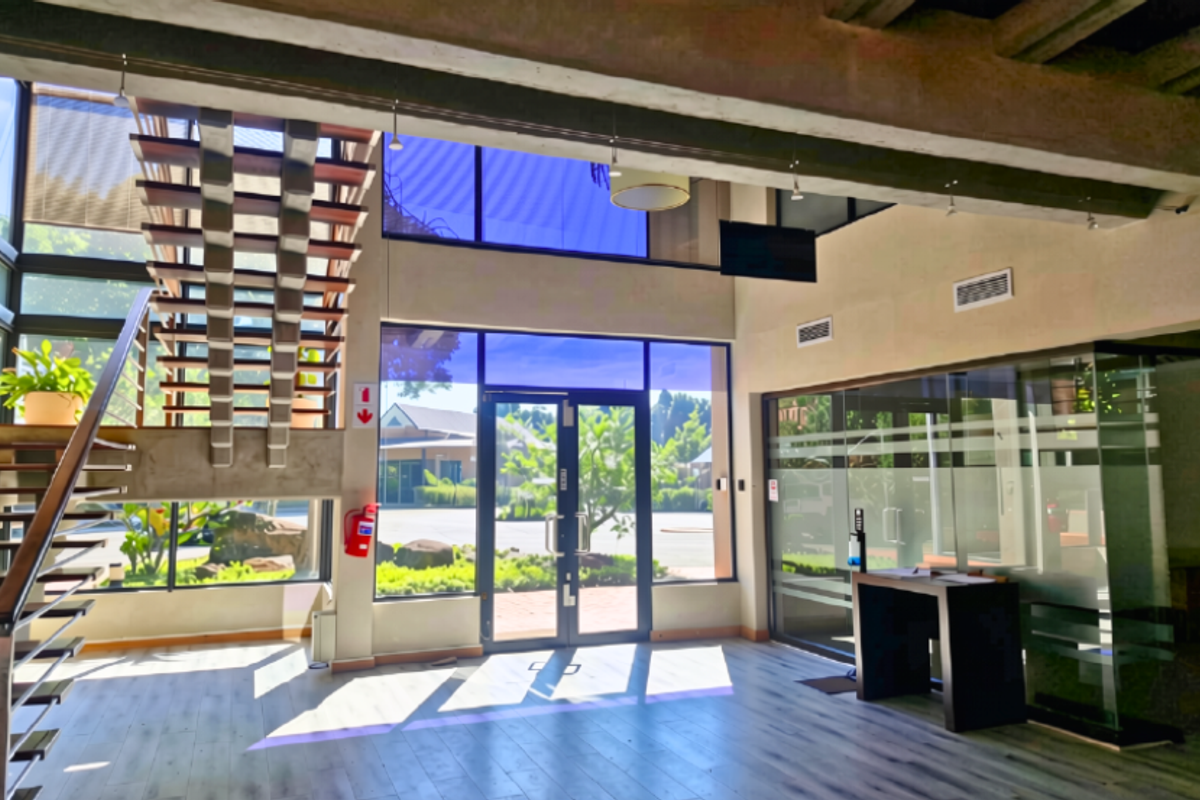 Spacious double-volume office entrance featuring a modern floating staircase, extensive glass curtain walling, and exposed concrete architectural elements.