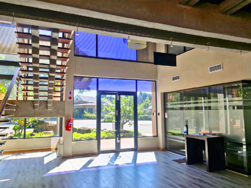 Spacious double-volume office entrance featuring a modern floating staircase, extensive glass curtain walling, and exposed concrete architectural elements.