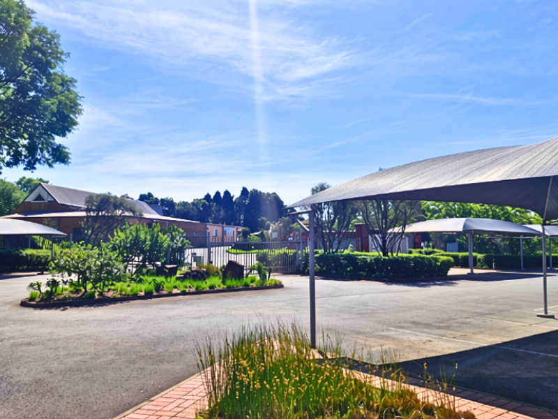Exterior view of the office property featuring a paved driveway, landscaped garden areas, and covered parking structures under a clear blue sky.
