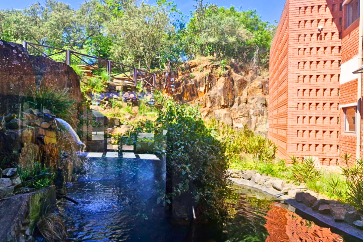 A landscaped rear exterior area featuring a natural rock face, a decorative water feature, and a modern brick office building facade.