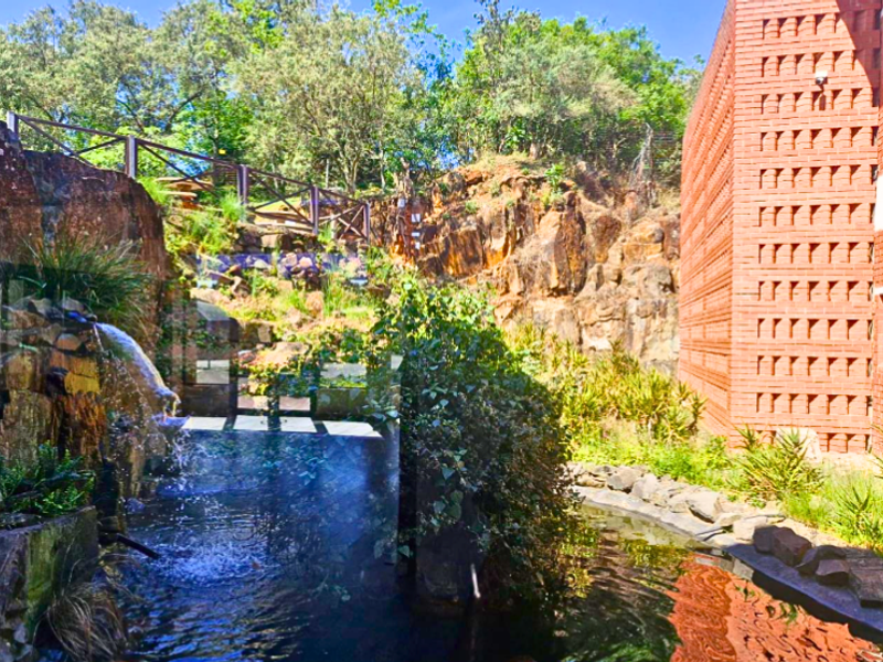 A landscaped rear exterior area featuring a natural rock face, a decorative water feature, and a modern brick office building facade.