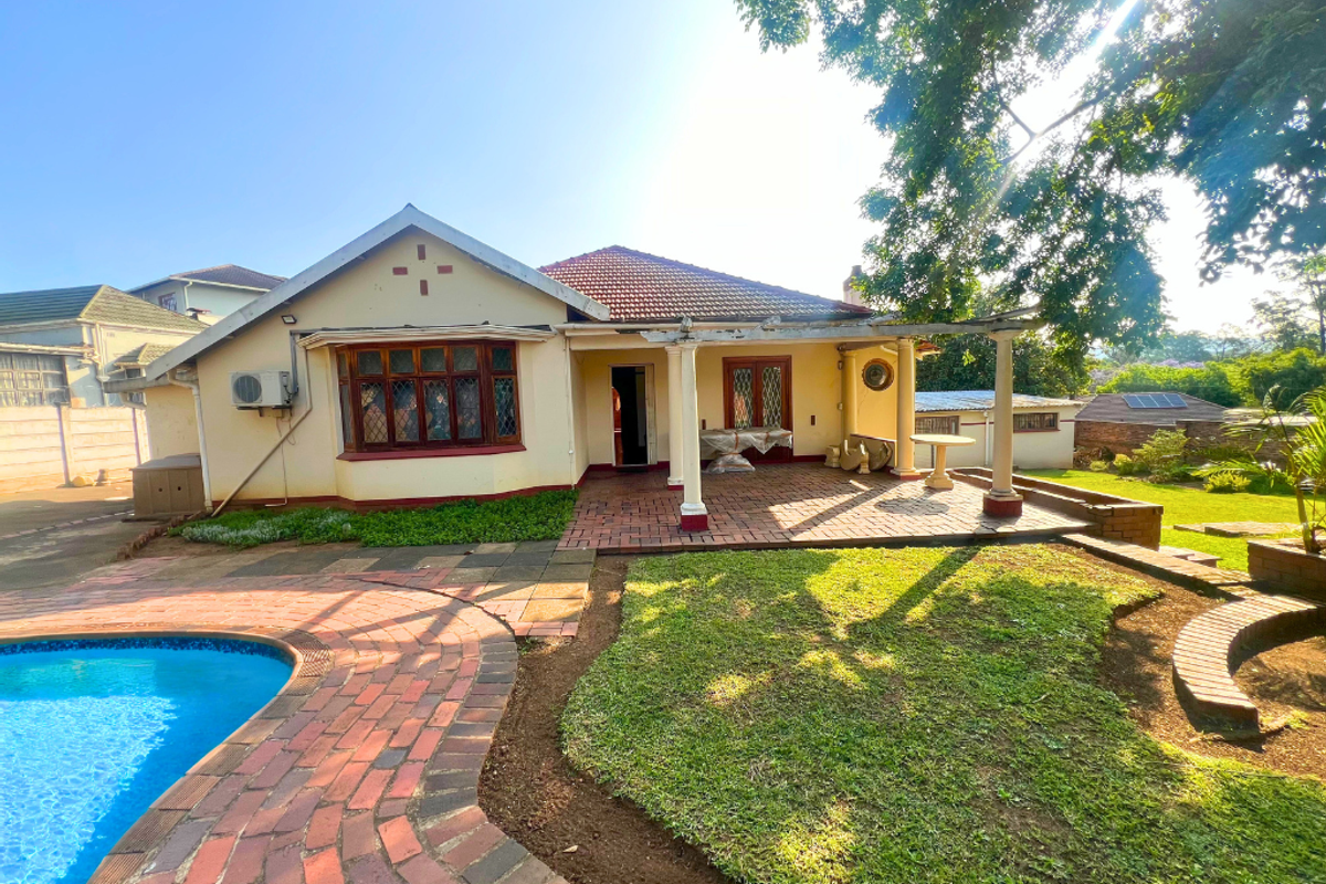 Rear view of the property featuring a covered patio, swimming pool, and landscaped garden area.