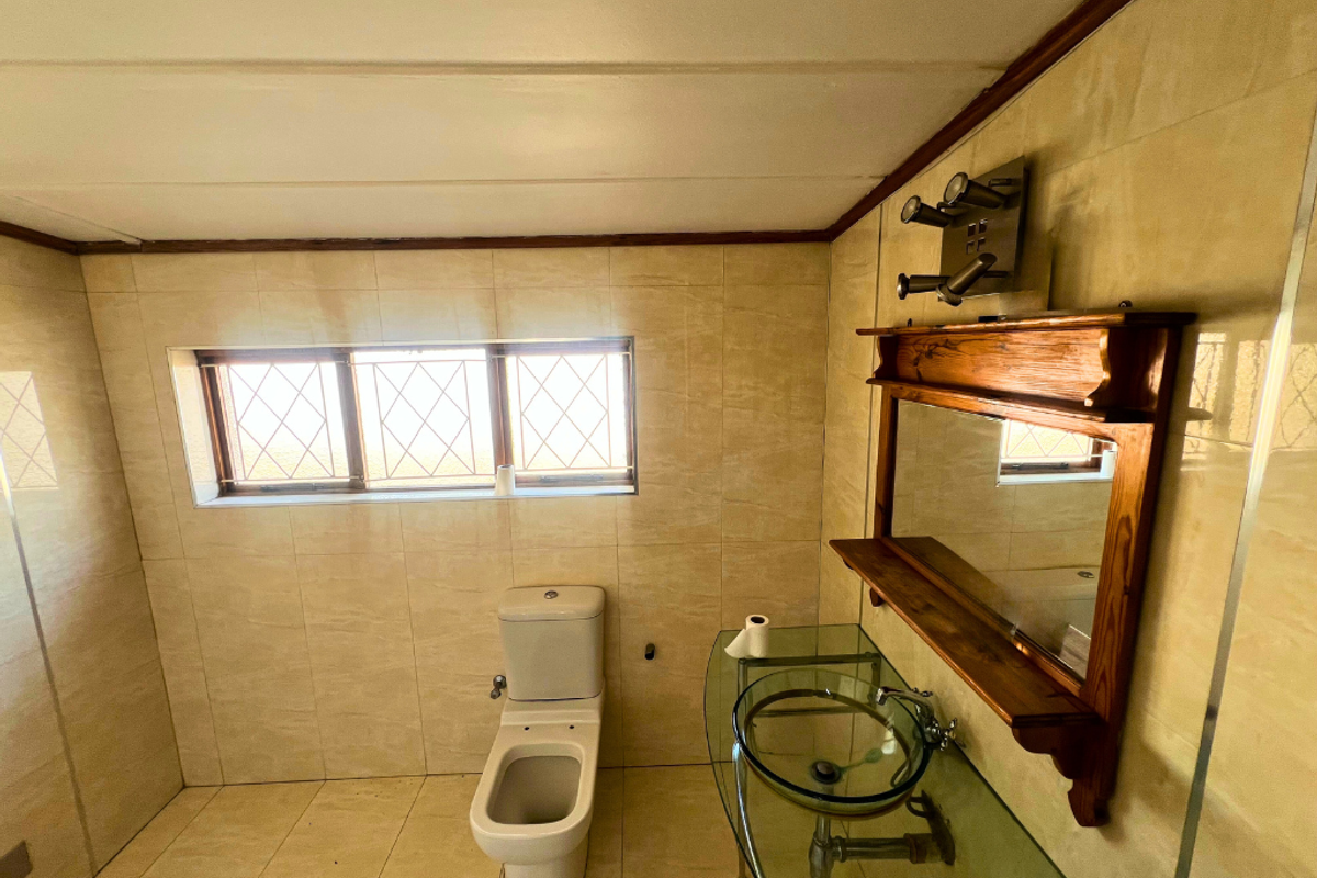 A functional bathroom featuring floor-to-ceiling beige tiling, a glass vessel sink with a wooden vanity mirror, and a standard toilet.
