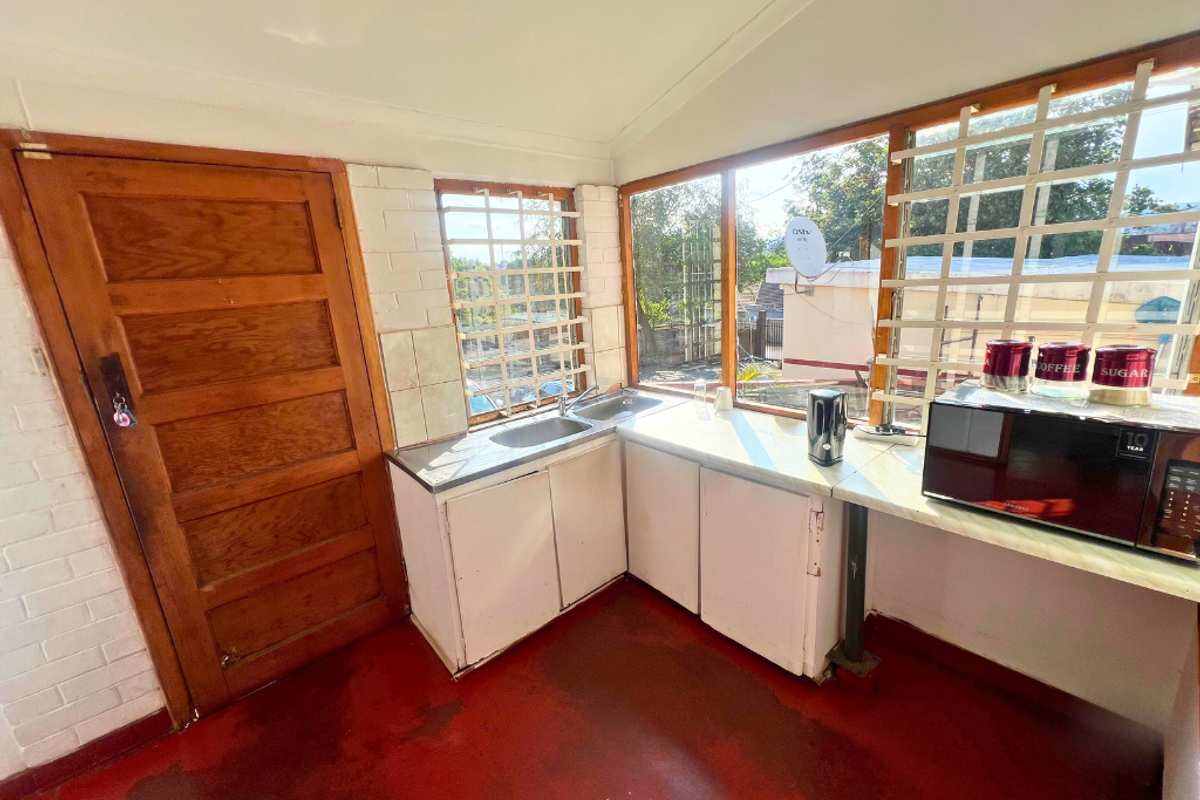 A compact kitchenette featuring built-in cabinetry, a stainless steel sink, and large windows with security bars, providing a functional workspace.