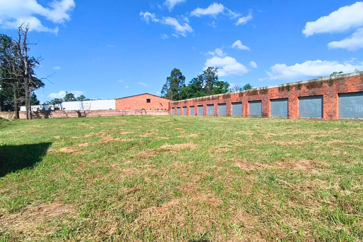 A large open industrial yard featuring a long row of brick storage units with roller shutter doors and perimeter walling.