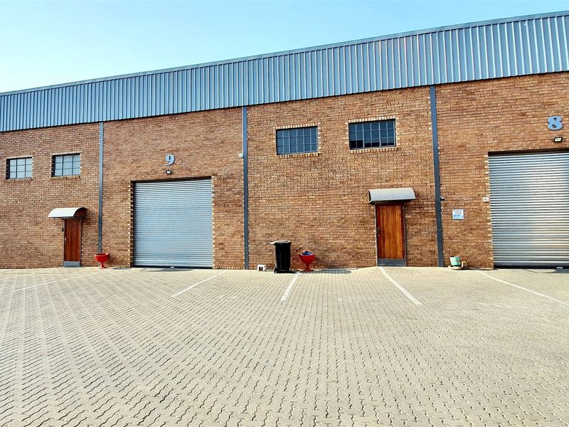 Front elevation of an industrial complex featuring brick facade, multiple metal roller shutter doors, and a paved parking area.