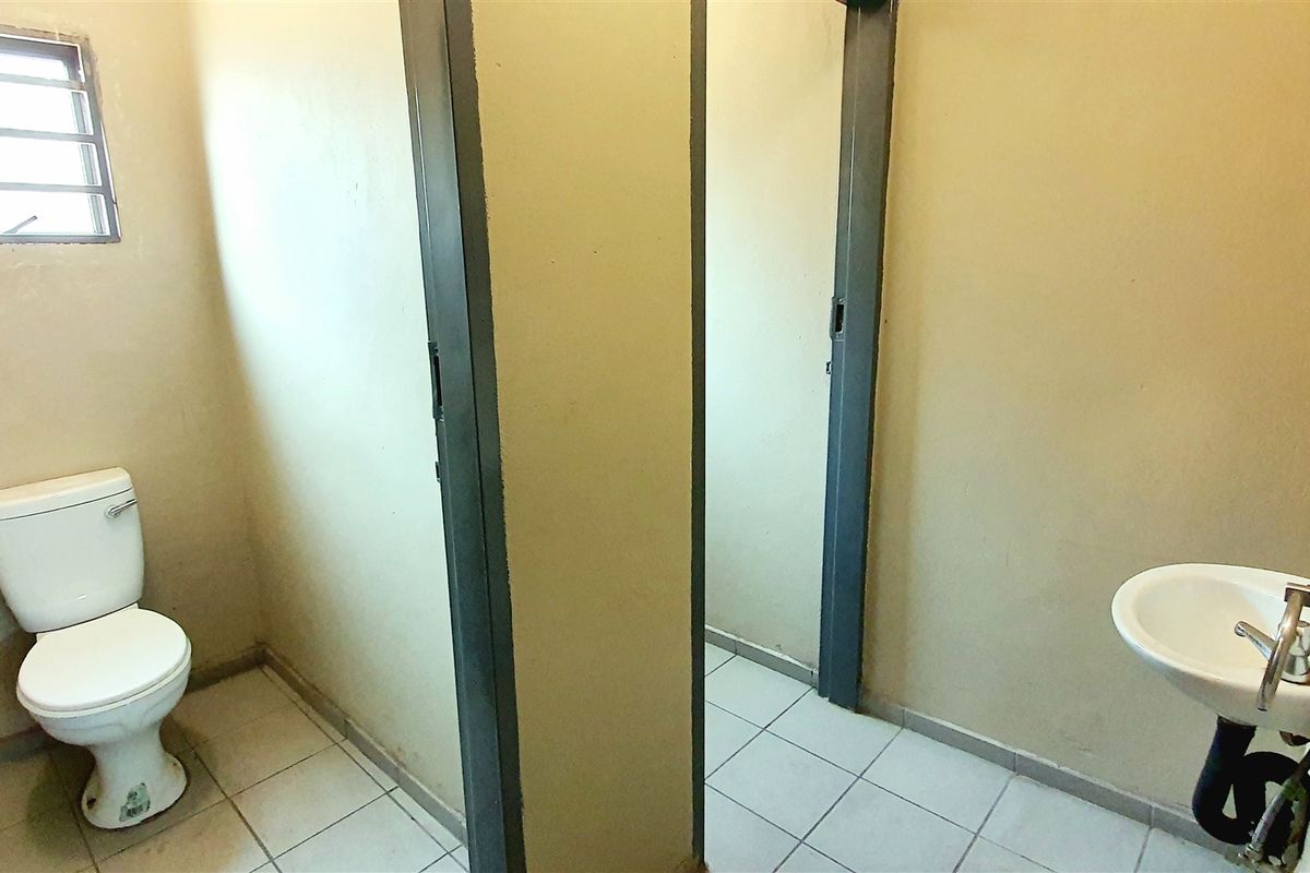 A functional industrial-style bathroom featuring a toilet, wall-mounted basin, and tiled flooring, requiring cosmetic updates to improve the overall finish.