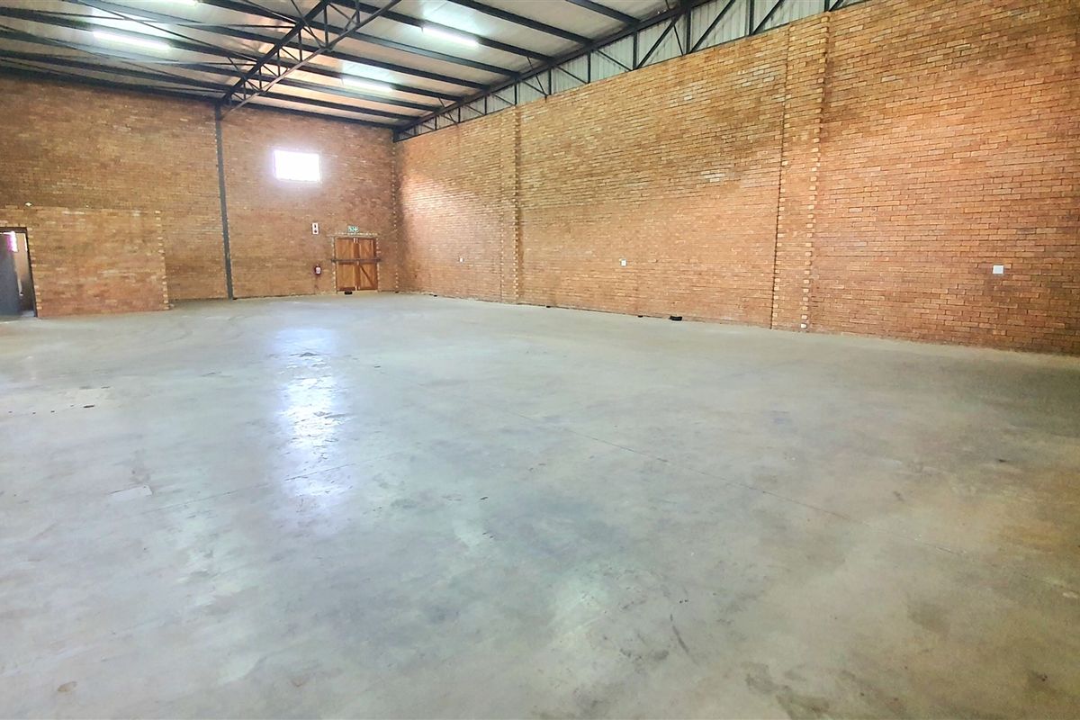 Spacious industrial warehouse unit featuring exposed brick walls, durable concrete flooring, and high-clearance steel roof trusses with overhead lighting.