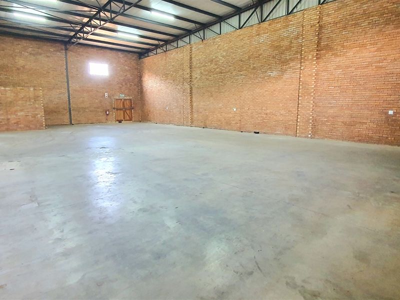 Spacious industrial warehouse unit featuring exposed brick walls, durable concrete flooring, and high-clearance steel roof trusses with overhead lighting.