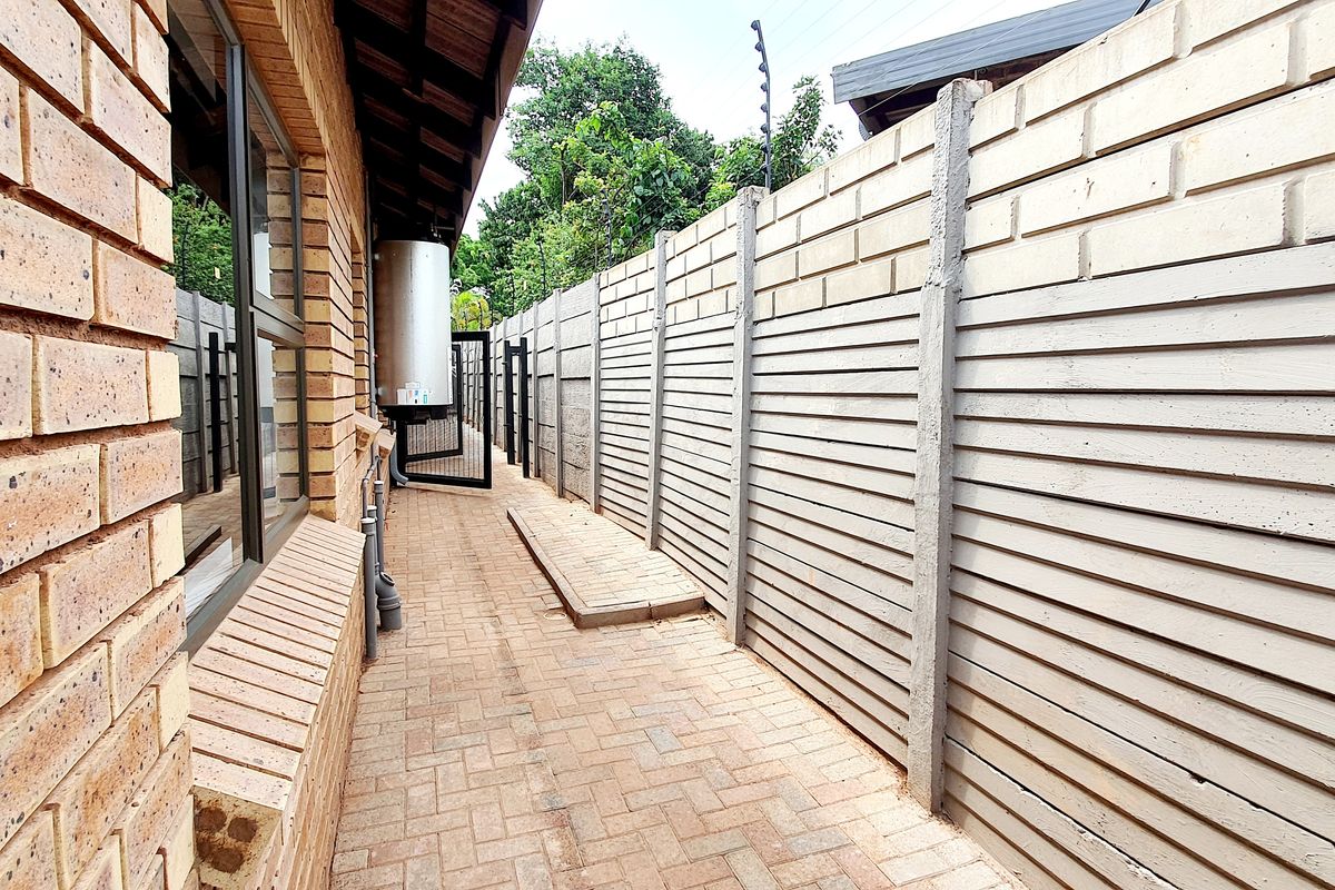 A side passage featuring brick paving, a precast concrete boundary wall with electric fencing, and an external geyser unit.