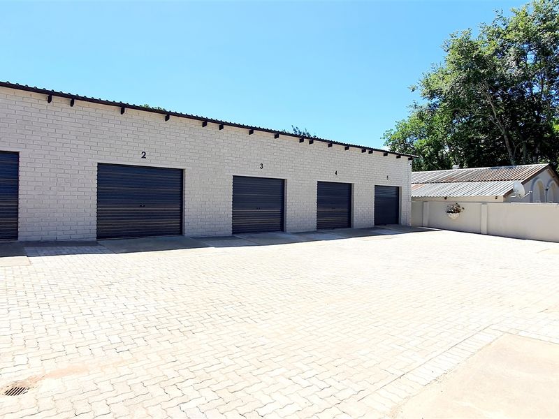 A well-maintained industrial property featuring a row of five secure roller shutter garage units with a spacious paved forecourt.