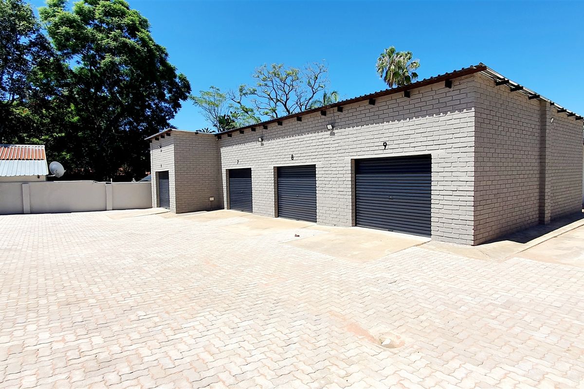 Industrial property featuring multiple roller shutter garage units with a spacious paved driveway and secure perimeter walling.