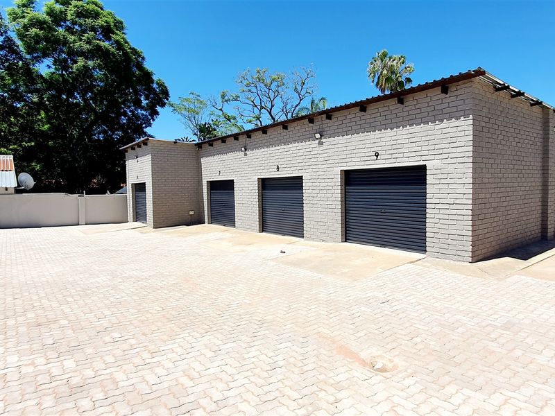 Industrial property featuring multiple roller shutter garage units with a spacious paved driveway and secure perimeter walling.