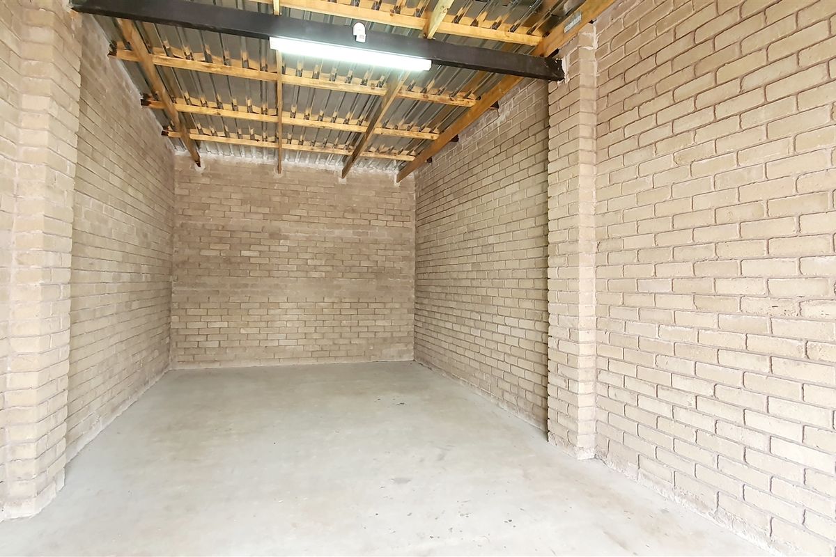A clean, industrial-style utility space or storage unit featuring exposed brick walls, concrete flooring, and an open timber-trussed ceiling with metal roofing.