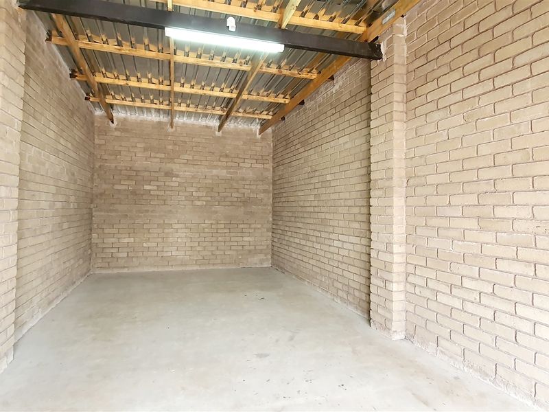 A clean, industrial-style utility space or storage unit featuring exposed brick walls, concrete flooring, and an open timber-trussed ceiling with metal roofing.