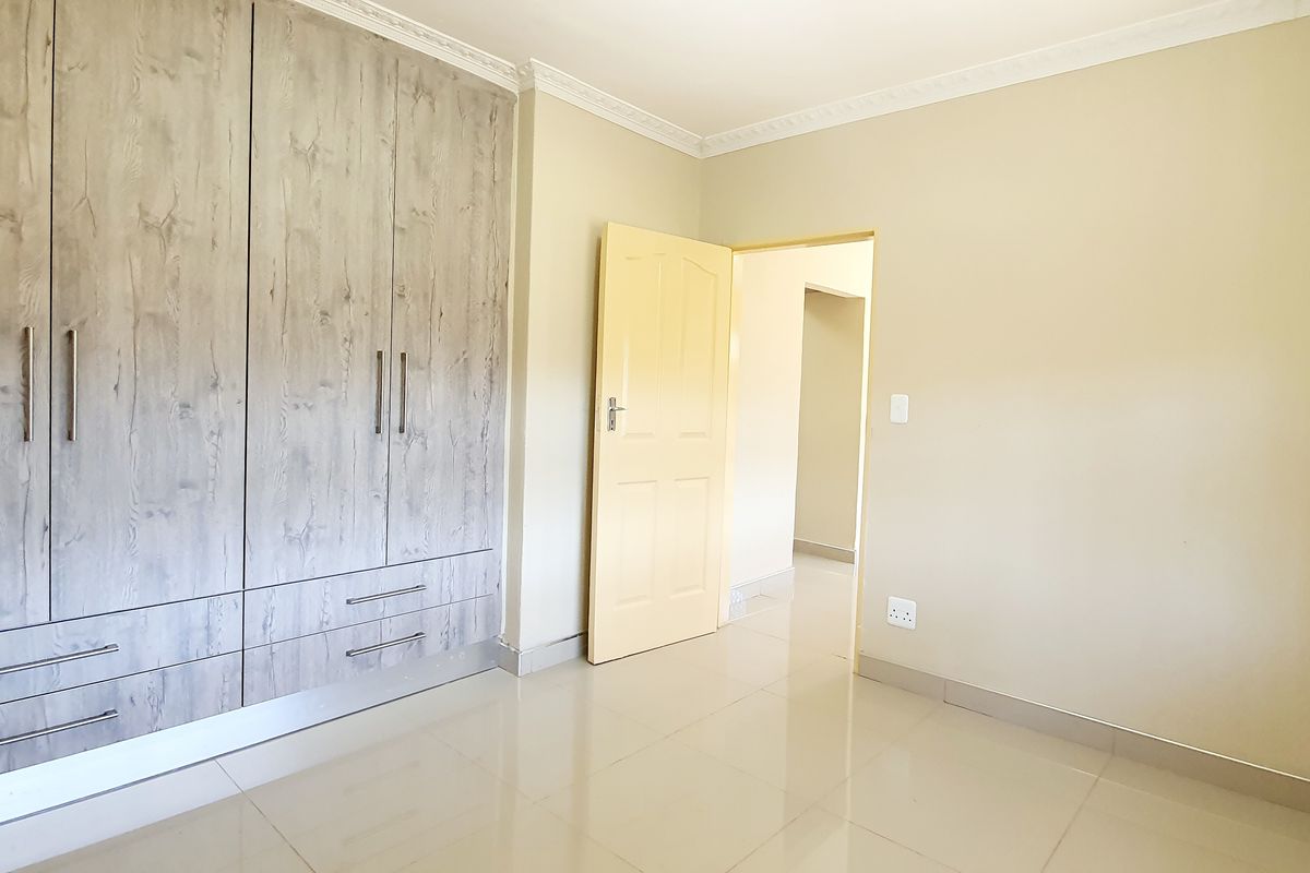 A bright bedroom featuring modern wood-grain built-in cupboards, tiled flooring, and decorative ceiling cornicing.
