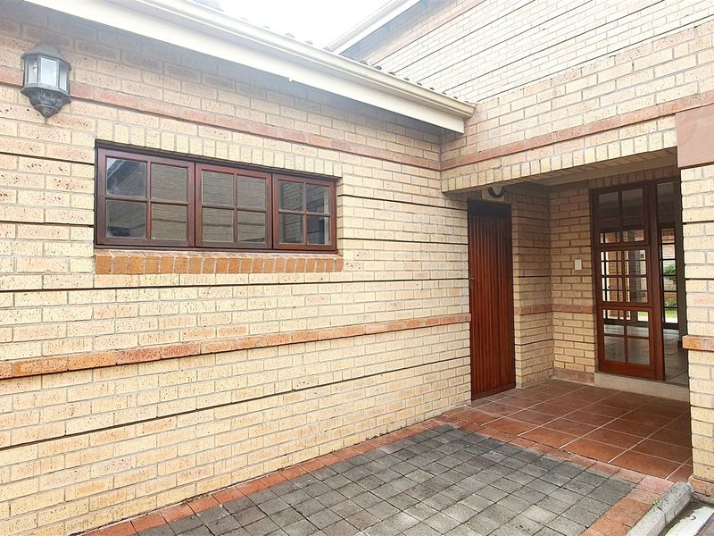 A rear exterior view of the townhouse featuring a face brick facade, paved courtyard area, and timber-framed door and window fixtures.