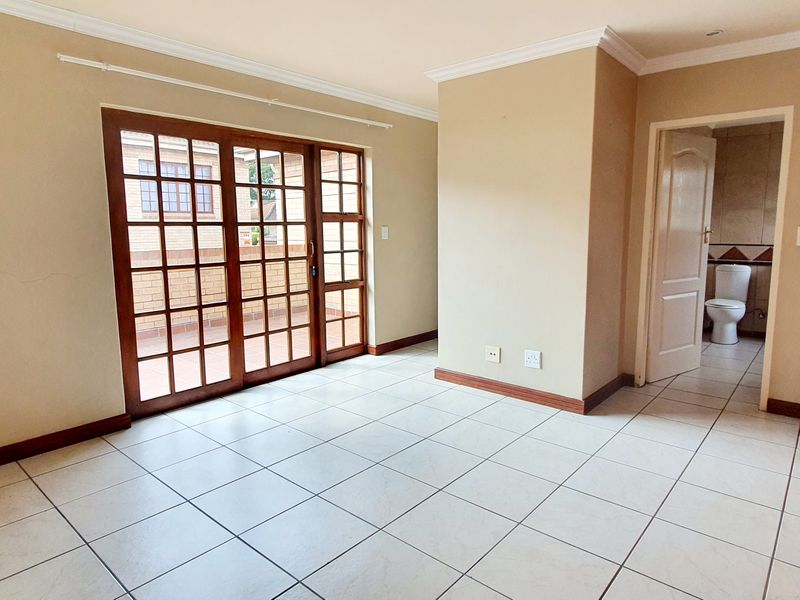 An empty bedroom featuring tiled flooring, built-in wooden wardrobes, and sliding glass doors leading to an outdoor area, with an en-suite bathroom visible.