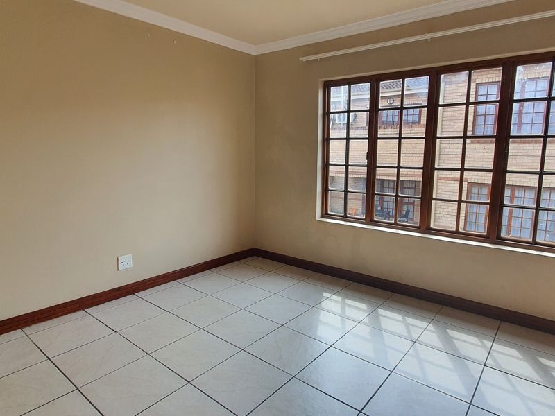 A bright, empty bedroom featuring tiled flooring, wooden window frames, and a built-in cupboard, offering a clean canvas for personalization.