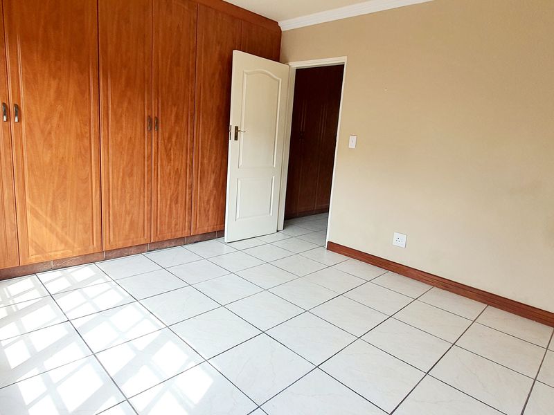 A bright, empty bedroom featuring tiled flooring and extensive built-in wooden cupboards, offering a clean and functional space ready for personalization.