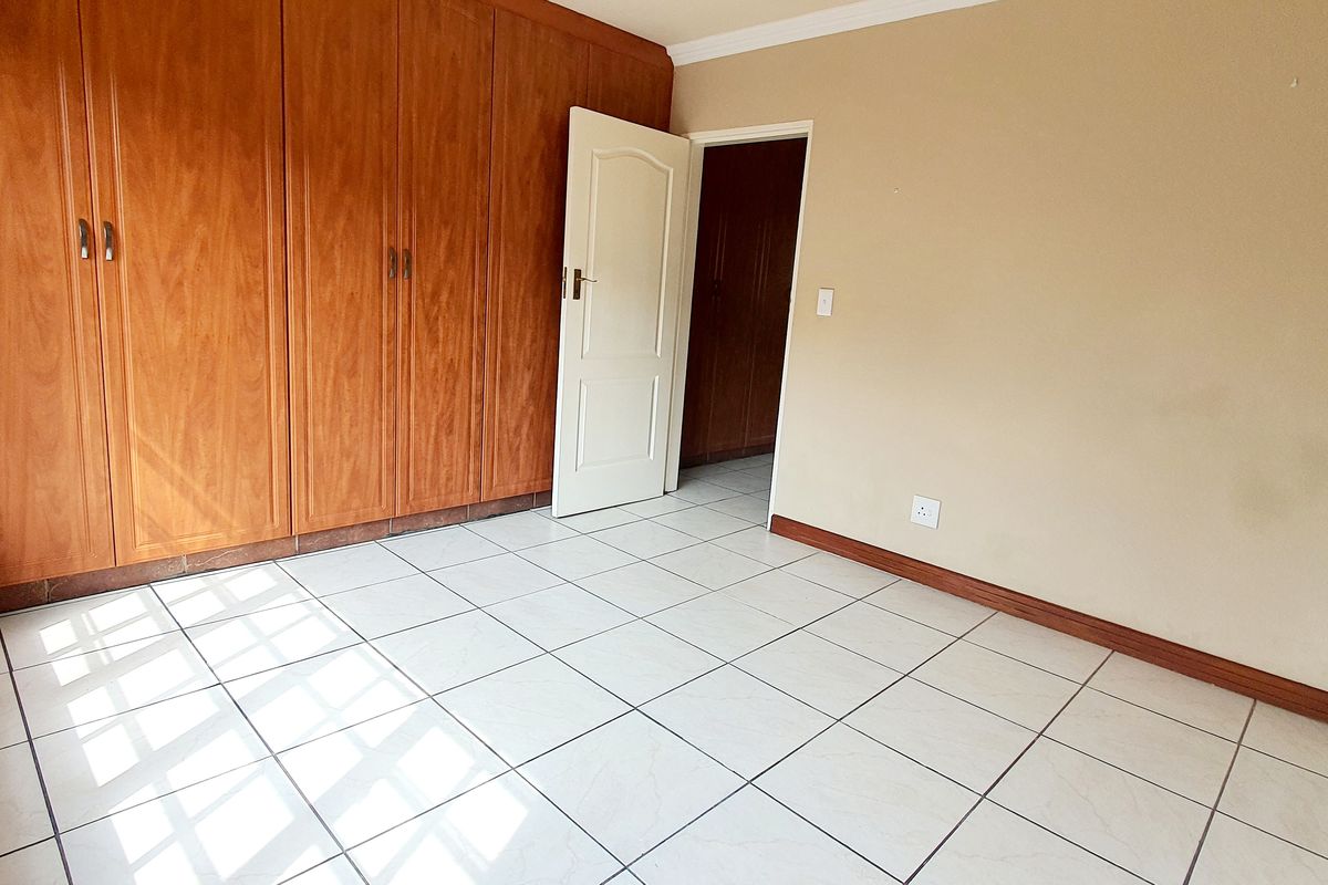 A bright, empty bedroom featuring tiled flooring and extensive built-in wooden cupboards, offering a clean and functional space ready for personalization.