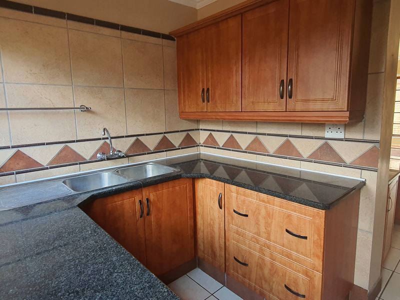 A functional kitchen featuring wooden cabinetry, granite countertops, a double bowl sink, and decorative tiled backsplash, leading into an open-plan living area.