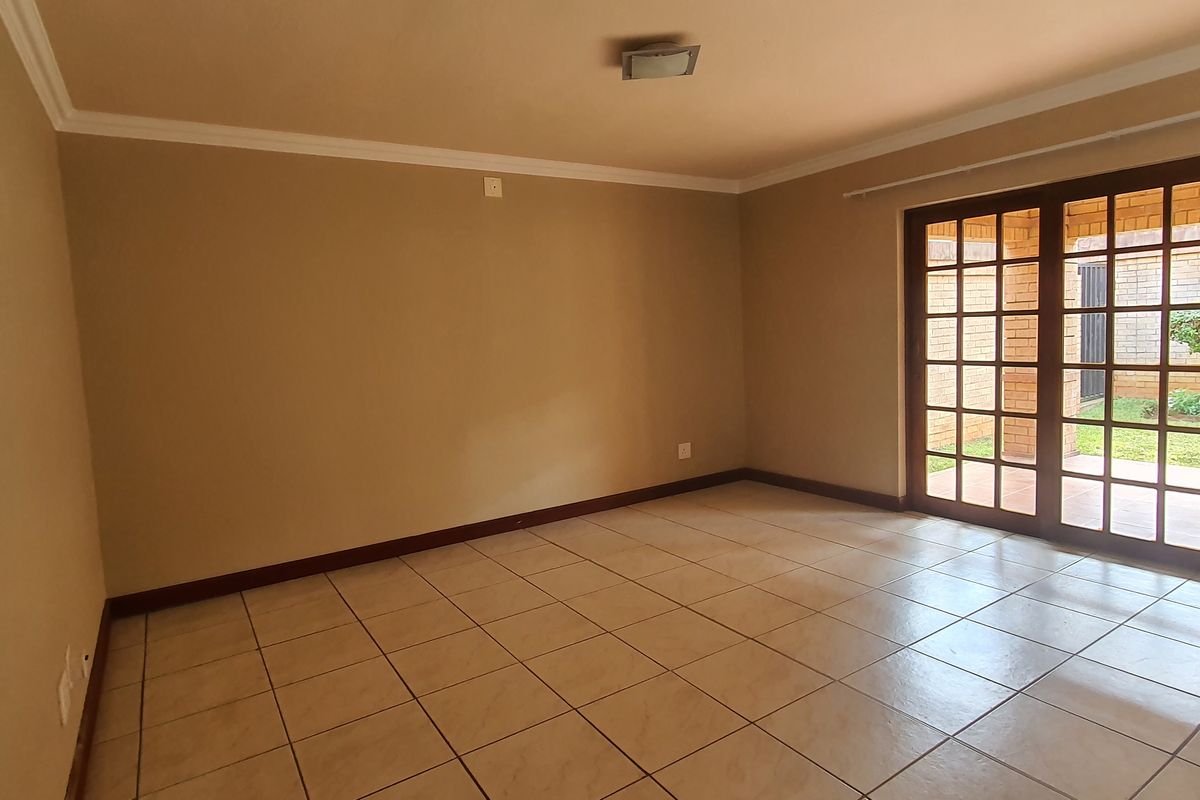An empty, neutrally painted living room featuring tiled flooring and large french doors that provide direct access to the outdoor patio area.