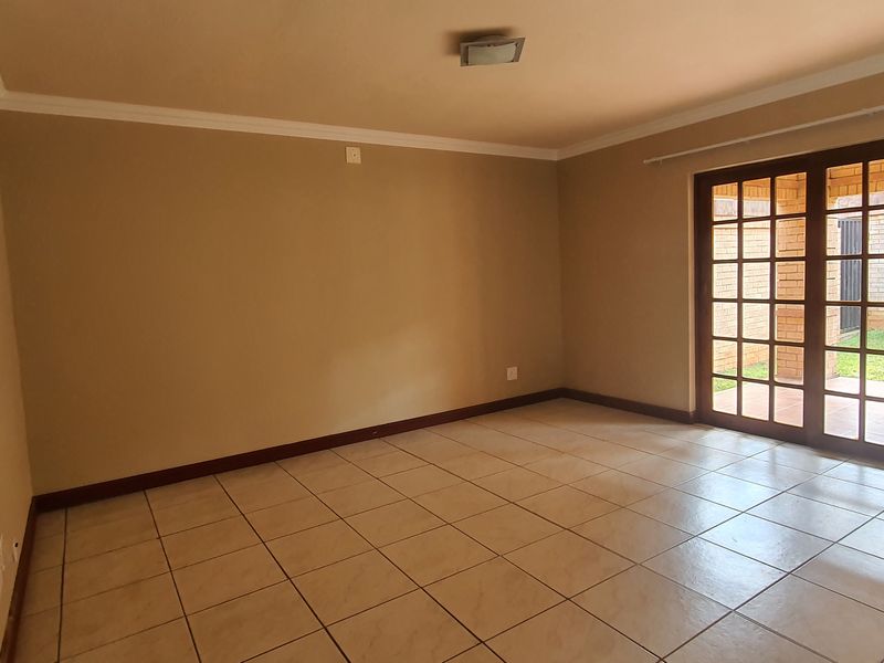 An empty, neutrally painted living room featuring tiled flooring and large french doors that provide direct access to the outdoor patio area.