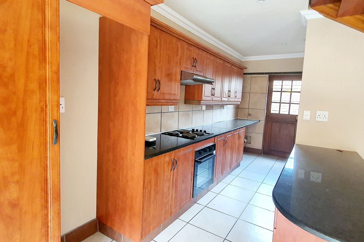 A functional kitchen featuring wooden cabinetry, granite countertops, a built-in oven with gas hob, and a breakfast bar area.