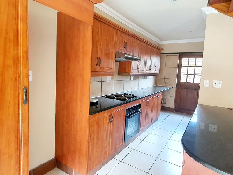 A functional kitchen featuring wooden cabinetry, granite countertops, a built-in oven with gas hob, and a breakfast bar area.