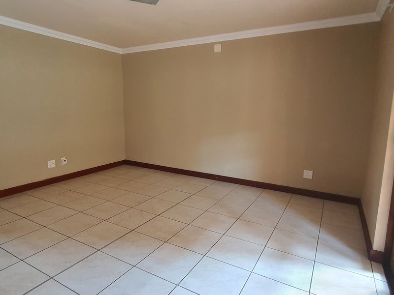 An empty, neutral-toned living room featuring tiled flooring, coving, and a wooden-framed glass door providing access to the exterior.