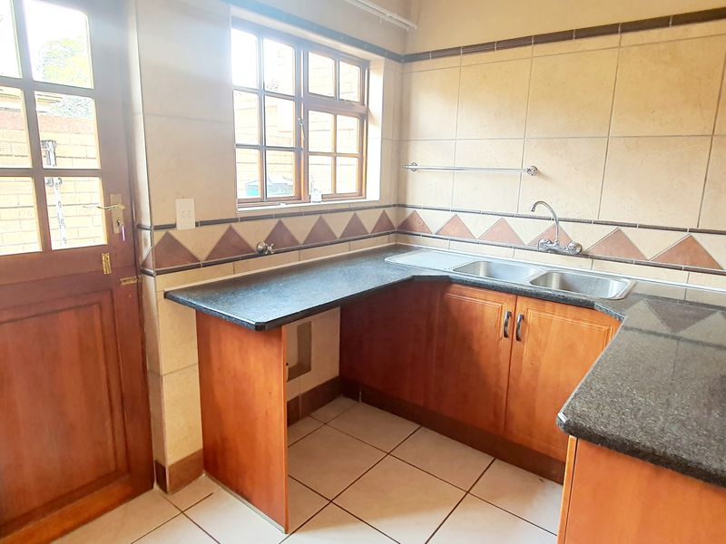 A functional kitchen featuring wooden cabinetry, granite countertops, a double bowl sink, and tiled splashbacks with direct access to the exterior.