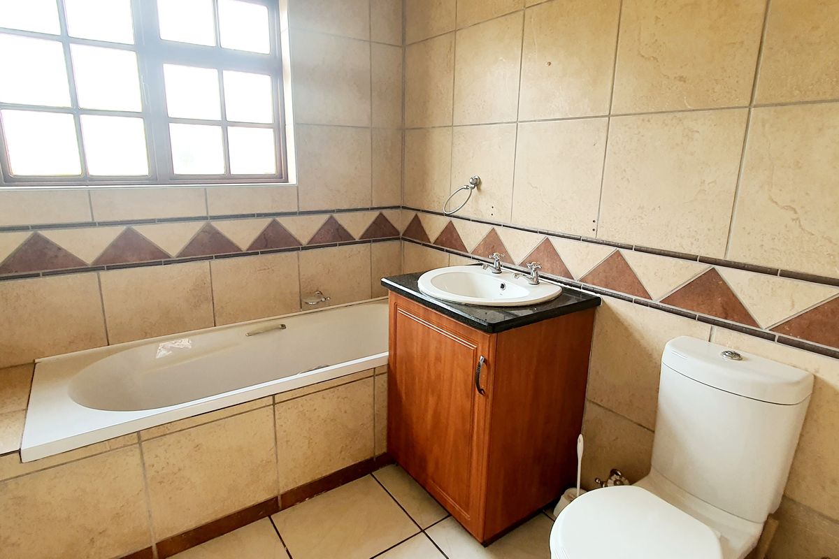 A functional bathroom featuring a built-in bathtub, vanity cabinet with granite countertop, and tiled finishes throughout.